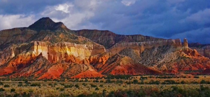 Light hitting the red foothills and layered pale tuff cliffs of Abiquiu, NM, under an overcast sky