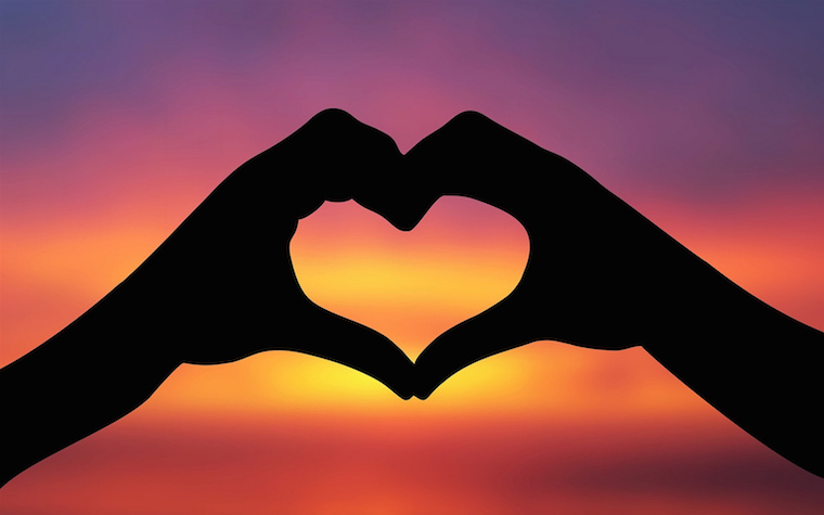 Silhouette of hands forming a heart shape against yellow, orange, and purple light